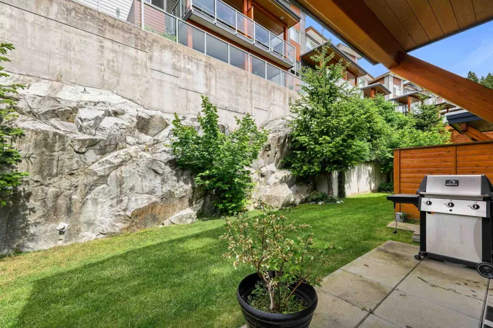 Private patio space featuring a paved surface, a lush lawn, and natural rock retaining walls