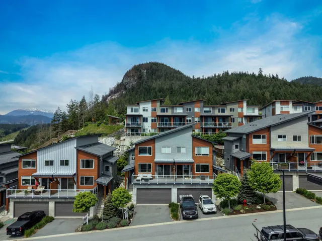Modern architecture townhomes featuring multiple balconies and attached garages, set against a backdrop of forested mountains