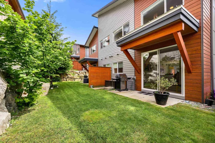 Rear exterior featuring wood siding, gray siding, a large sliding glass door, an overhang with wood supports, and a grassy lawn