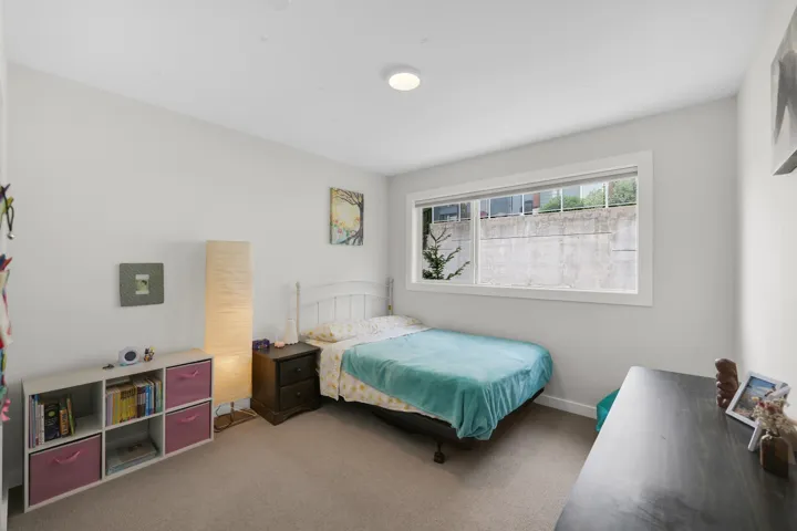 Bright bedroom featuring light gray walls, a window with white trim, and neutral-toned carpeting