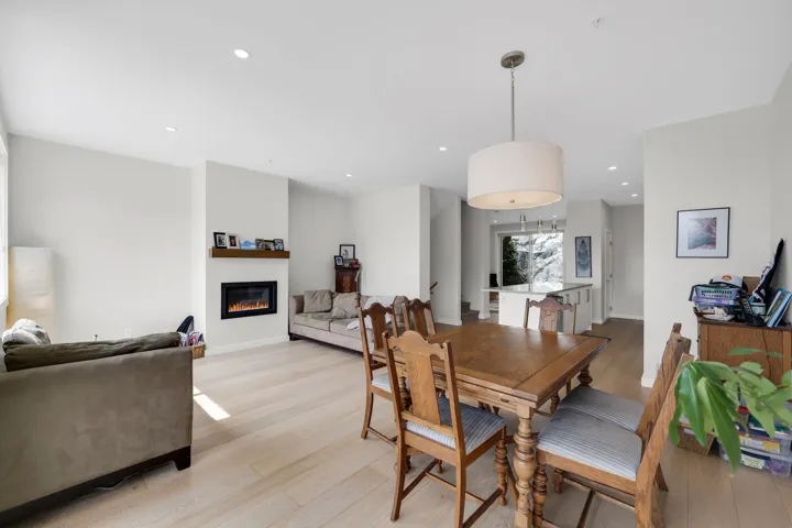 Open-concept living area with light wood-finish flooring, recessed lighting, and a modern fireplace with a wood mantle