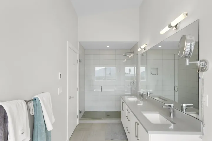 Spacious bathroom featuring a dual vanity with undermount sinks, substantial mirror, glass-enclosed shower, and light-toned tile flooring
