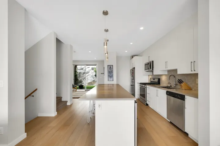 Open-concept kitchen with a long island featuring pendant lighting, white cabinetry, stainless steel appliances, and wood-finish flooring