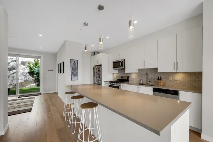 Modern kitchen featuring a long island with a light-toned countertop, white cabinetry, stainless steel appliances, and wood-finish flooring