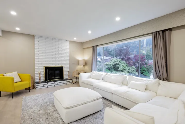 Living room featuring a floor-to-ceiling painted brick fireplace with a raised hearth, expansive picture window, recessed lighting, and wood-finish flooring