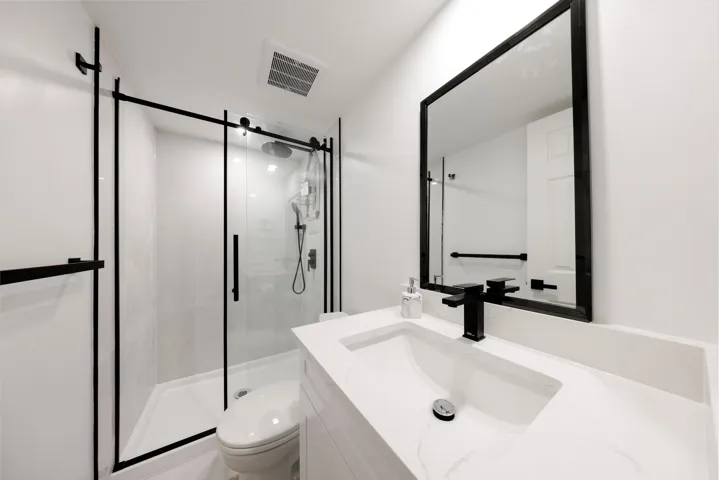 Bathroom featuring a vanity with a white countertop and rectangular undermount sink, matte black faucet, glass-enclosed shower with matte black hardware, and a matching framed wall mirror