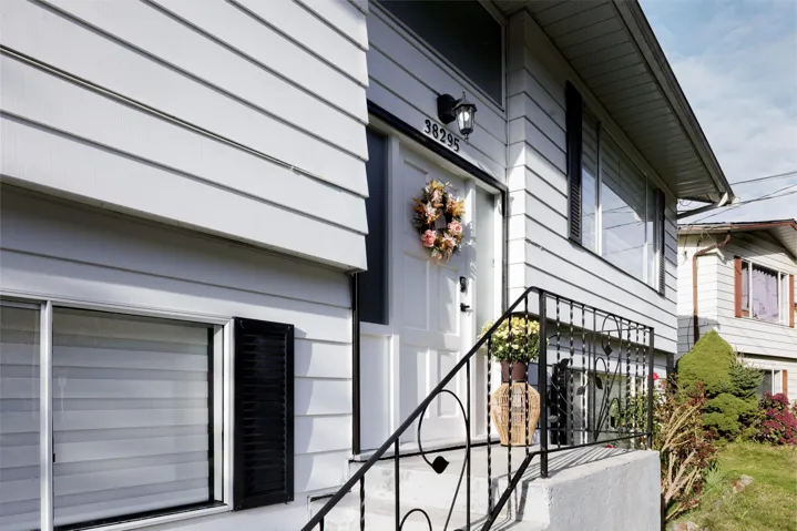 Exterior entry featuring light-colored horizontal lap siding, white-paneled front door, custom metal handrailing, and dark-finished decorative window shutters
