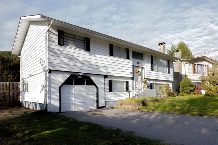 Two-story residence featuring white horizontal siding, contrasting black shutters, an integrated one-car garage, and a masonry chimney