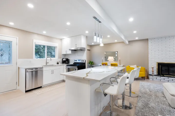 Kitchen featuring white cabinetry, a center island with a stone-finish countertop, stainless steel appliances, wood-finish flooring, and a painted brick fireplace