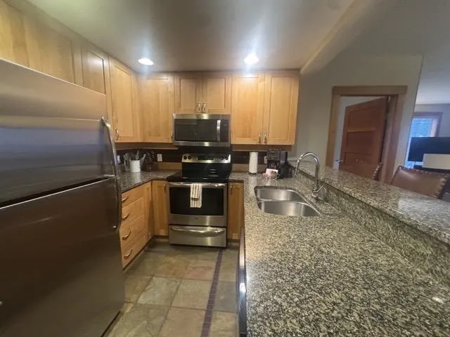 Kitchen with stainless steel appliances, dark stone counters, recessed lighting, and a peninsula