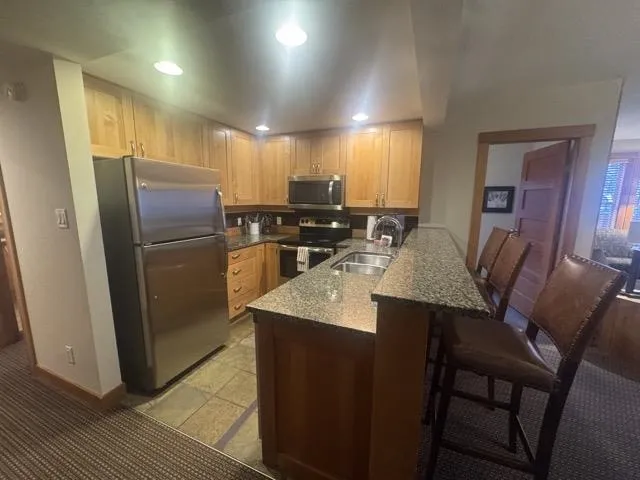 Kitchen featuring stainless steel appliances, dark stone counters, a kitchen breakfast bar, a peninsula, and light wood finish cabinets