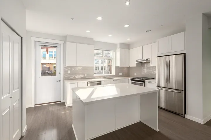 Modern kitchen featuring an island with a light-toned countertop, white cabinetry, stainless steel appliances, wood-finish flooring, and recessed lighting