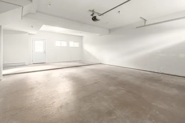 Spacious concrete-floored garage featuring a white door, three transom windows, a garage door opener, and white painted walls