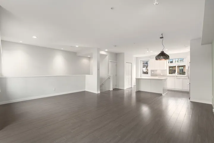 Open-concept living space featuring wood-finish flooring, recessed lighting, a modern pendant light, white kitchen cabinetry, and a kitchen island with a light-colored countertop