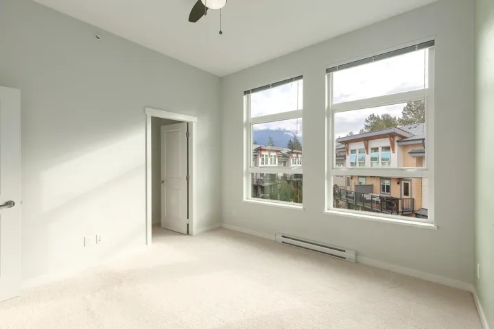 Light-colored carpeting complementing soft gray walls, featuring two large windows with blinds, a ceiling fan, and white trim throughout