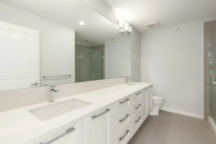 Double vanity with integrated sinks, contemporary chrome faucets, and white shaker-style cabinetry