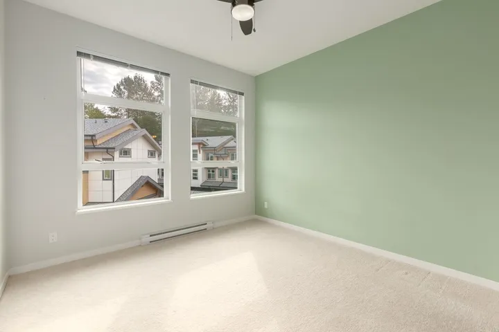 Room featuring light green and off-white painted walls, light-toned carpet flooring, and two large windows with horizontal blinds