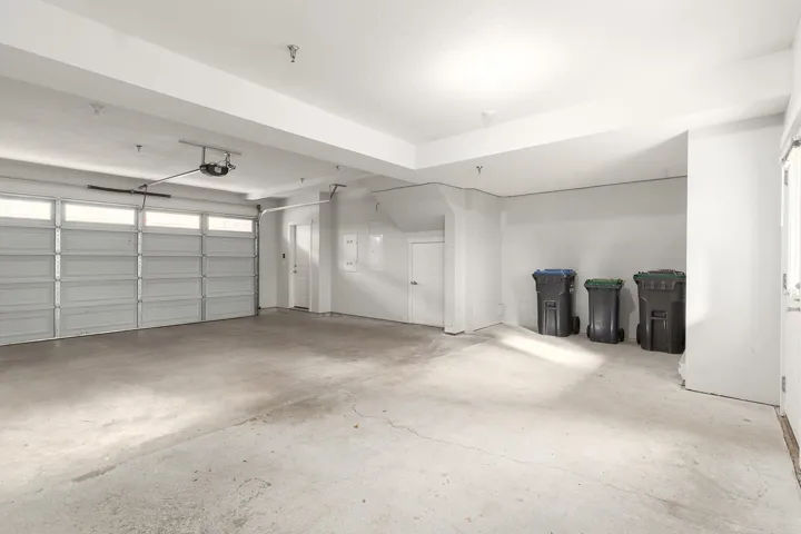 Spacious garage with concrete flooring, a paneled garage door with upper light panels, automatic opener, and a side door entry