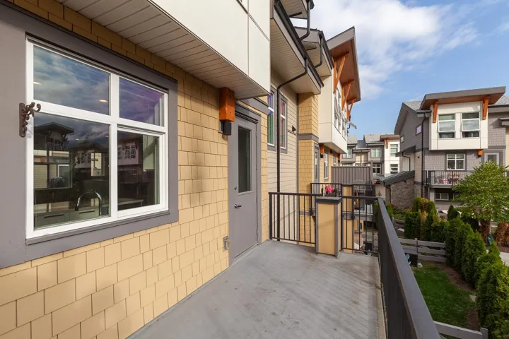 Private concrete balcony with black metal railings, featuring wood-shingle siding and a white-framed window