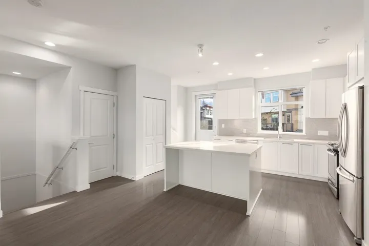 Open-concept kitchen featuring an island, integrated stainless steel appliances, white cabinetry, and a light-toned backsplash