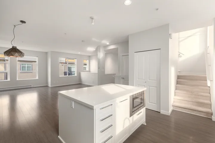 Open-concept living space featuring a central kitchen island with a built-in microwave, wood-finish flooring, recessed lighting, and multiple windows