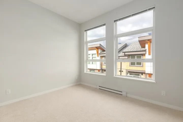 Neutral-toned room featuring a light-colored carpet, white baseboards, and two large windows with white frames