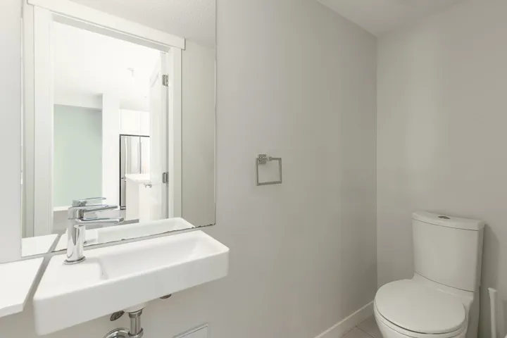Powder room featuring a wall-mounted rectangular sink with a chrome faucet, a frameless wall mirror, and a white toilet