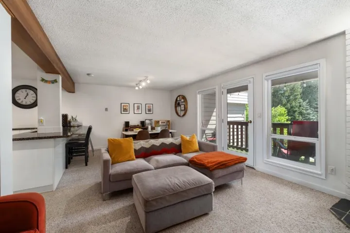 Carpeted living area featuring a wood-finish ceiling beam, built-in breakfast bar with a dark countertop, white trim, and a door opening to an outdoor deck