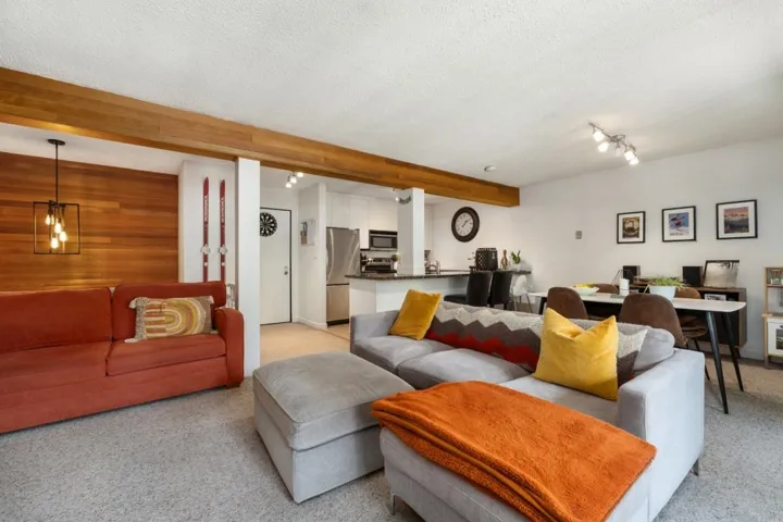 Open-concept living area featuring a wood plank accent wall, exposed wood beam, recessed lighting, and track lighting
