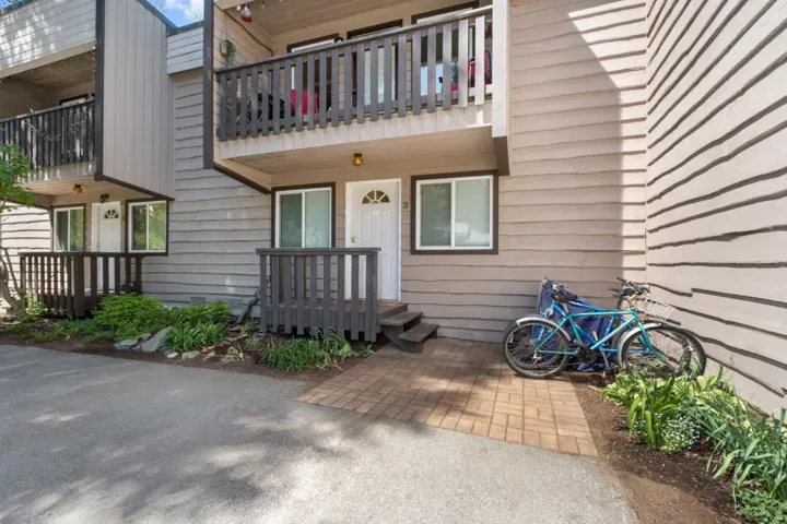 Two-story exterior with horizontal siding, dark trim accents, private balcony, ground-level patio, and brick paver walkway
