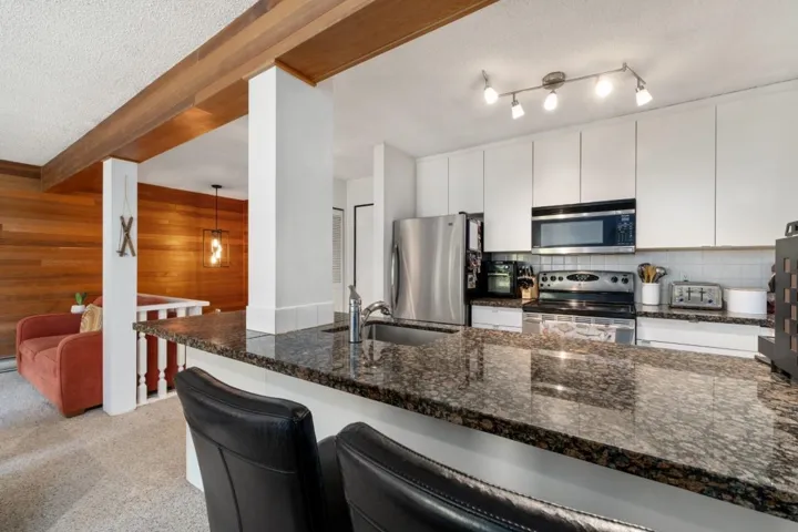 Kitchen featuring granite-style countertops, stainless steel appliances, white cabinetry, a tile backsplash, and track lighting