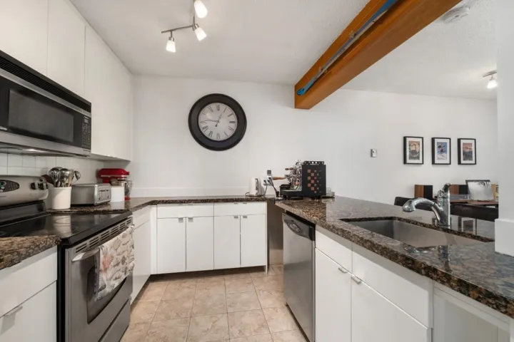 Kitchen featuring white cabinetry, dark granite-finish countertops, stainless steel appliances, and track lighting