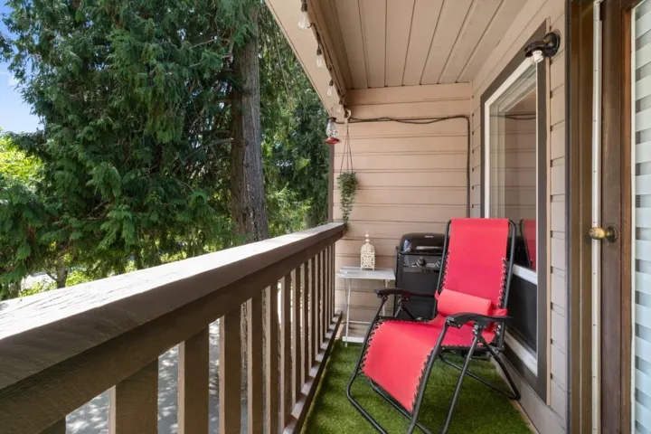 Exterior balcony featuring wood railing and siding, wall-mounted light fixture, and visible tree canopy