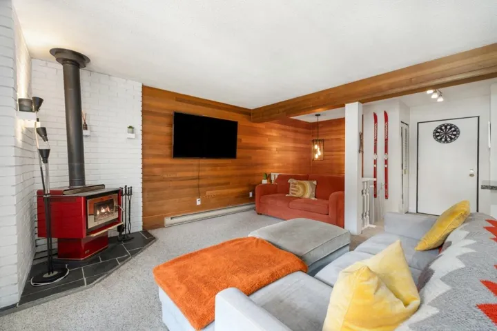 Living area featuring a red wood-burning stove with a slate hearth, white brick wall, wood-paneled accent wall, and exposed wood beam