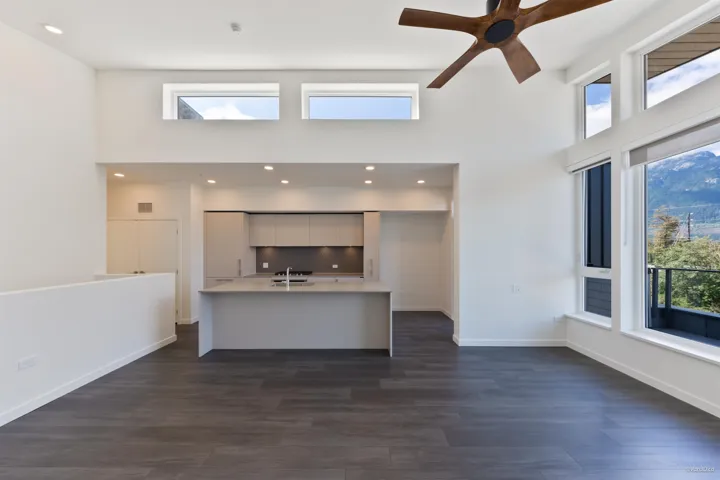 Open-concept living area with high ceilings, wood-finish flooring, a modern kitchen island, and extensive windows