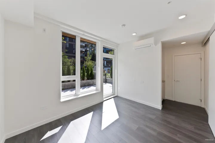 Bright interior with large windows and a glass-paneled door, recessed ceiling lighting, wood-finish flooring, and a wall-mounted air conditioning unit