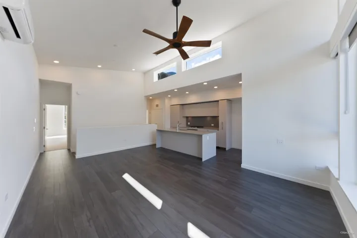 Open-concept living area with high ceilings, wood-finish flooring, a modern kitchen with an island, and large windows