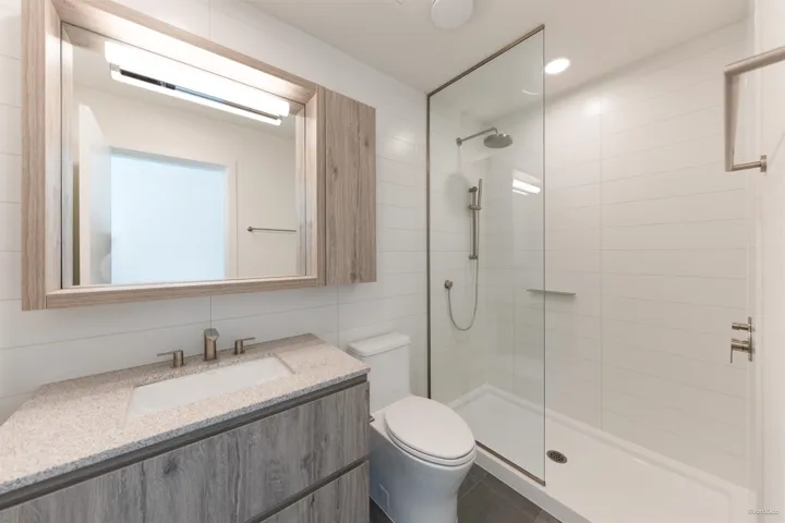 Modern bathroom featuring a wood-finish vanity with a light-toned countertop, a built-in shower with a glass enclosure, a rain showerhead, and white subway tile surround