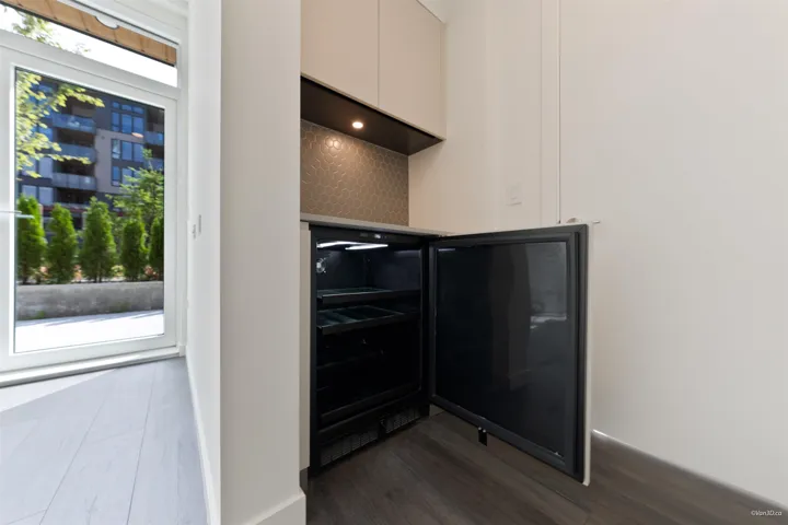 Built-in beverage refrigerator, patterned backsplash, under-cabinet lighting, wood-finish flooring, and white exterior door