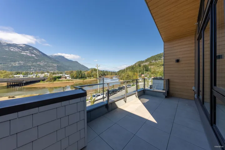 Outdoor balcony with tile flooring, glass railing, wood-finish siding, and large windows