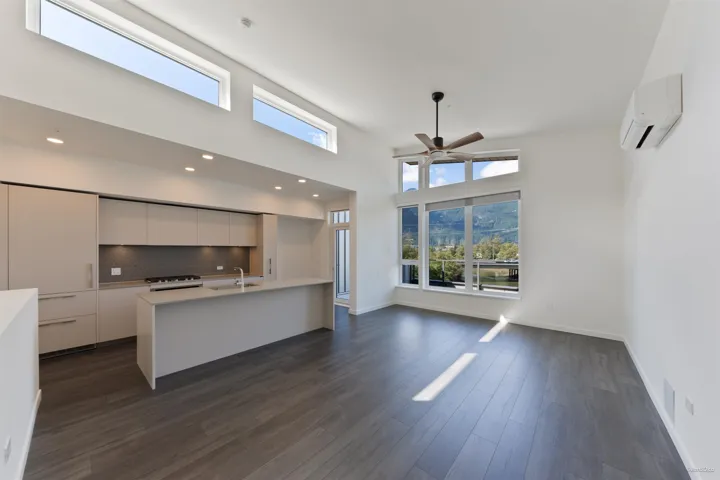 Open-concept living space featuring wood-finish flooring, a contemporary kitchen with integrated appliances and a center island, high ceilings with clerestory windows, and a ceiling fan