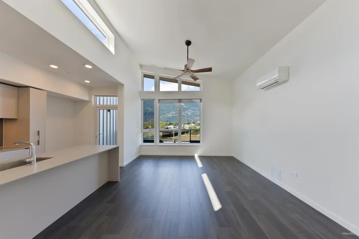 Vaulted ceiling with a ceiling fan, wood-finish flooring, and a contemporary kitchen island with an integrated sink