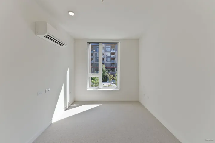 Neutral wall finishes, recessed ceiling lighting, window with white frame, wall-mounted climate control unit, and light-toned carpeting