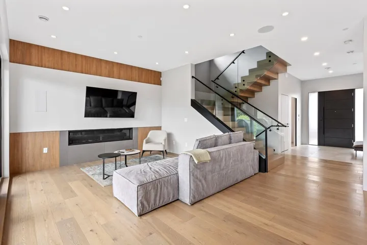 Living area with light wood-style flooring, stairs, a glass covered fireplace, and recessed lighting