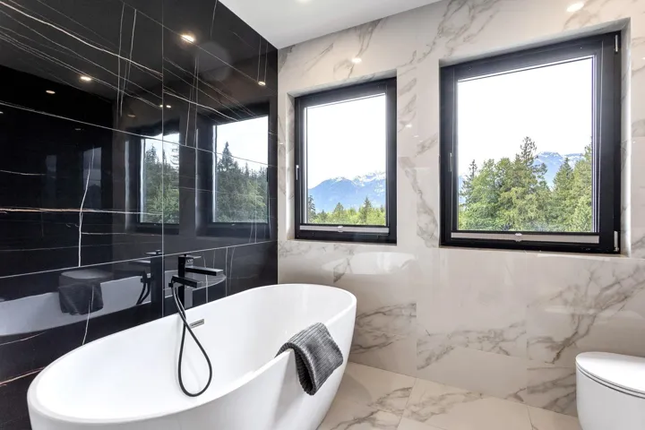 Bathroom with tile walls, marble tiled floors, a soaking tub, and toilet