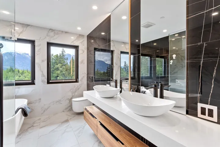 Full bath with a freestanding bath, double vanity, marble tiled floors, toilet, and stone wall