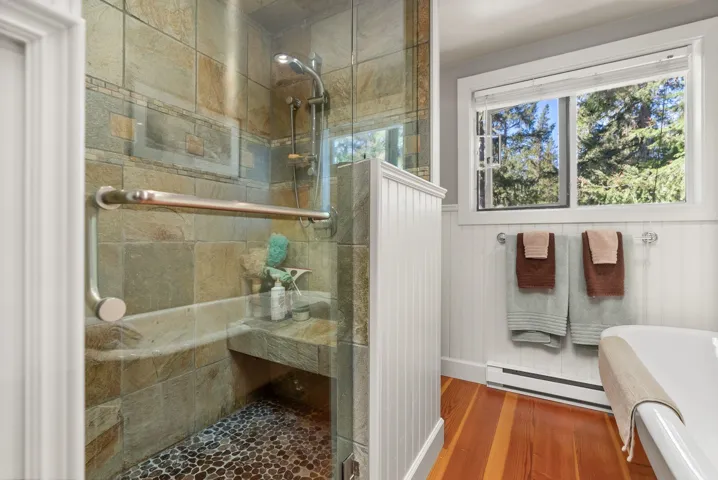 Full bath featuring a stall shower, baseboard heating, wood finished floors, and a wainscoted wall