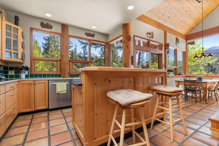 Kitchen featuring vaulted ceiling, dishwasher, a kitchen bar, decorative light fixtures, and glass insert cabinets