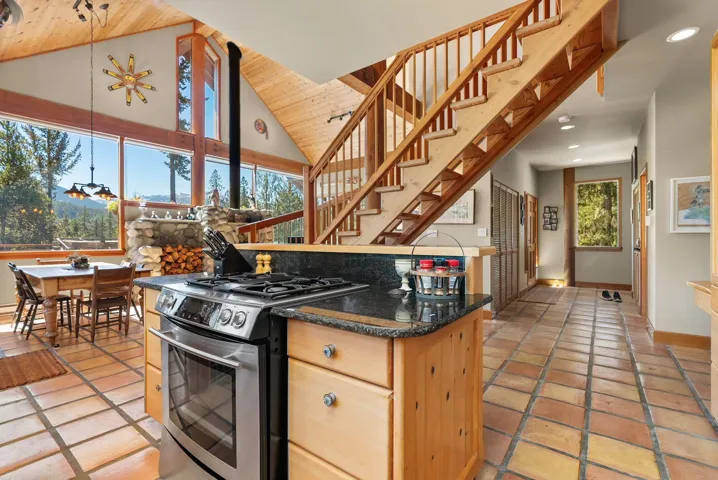Kitchen with gas stove, high vaulted ceiling, light brown cabinets, dark stone countertops, and wooden ceiling
