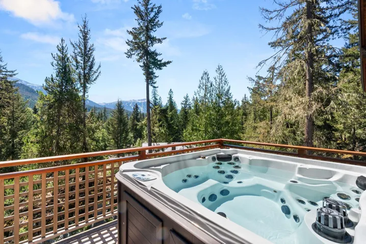 Wooden deck featuring a hot tub, a wooded view, and a mountain view